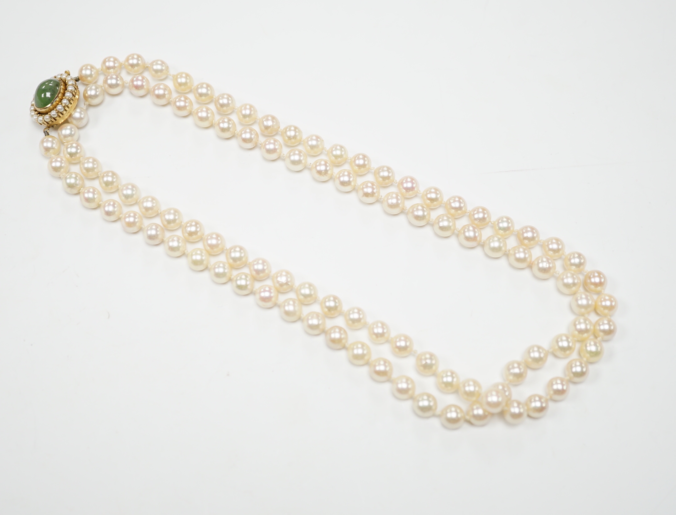 A Portuguese single strand cultured pearl necklace, with cabochon nephrite and seed pearl cluster set yellow metal clasp, 86cm.